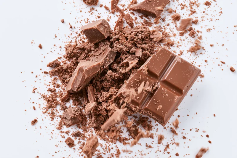 Broken milk chocolate bar pieces scattering midair on white background