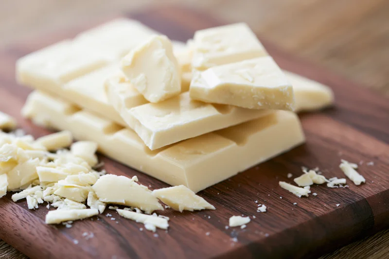Broken white chocolate bar pieces stacked and scattered on a wooden cutting board