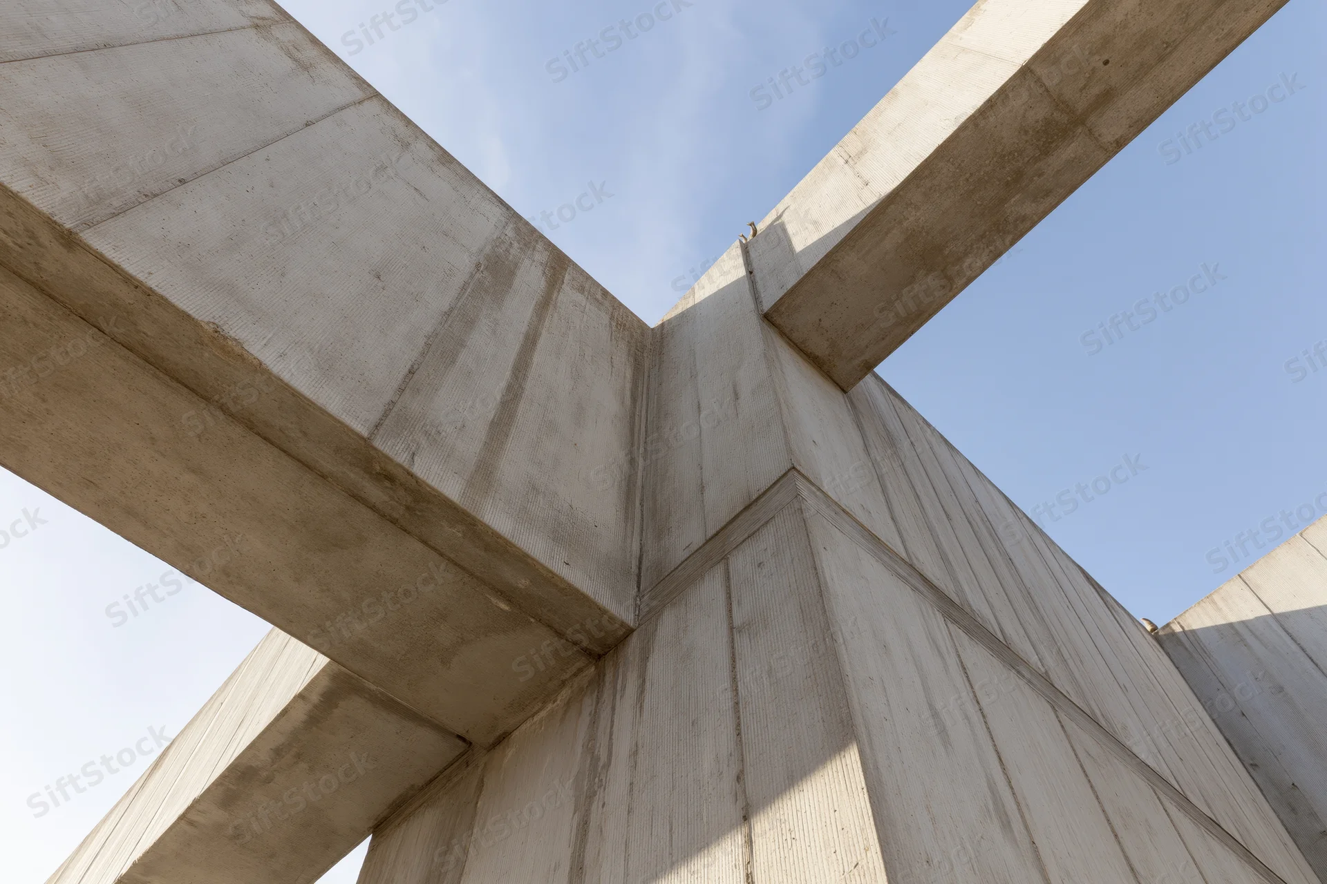 Brutalist concrete structure viewed from low angle showing intersecting beams and corner joint against blue sky