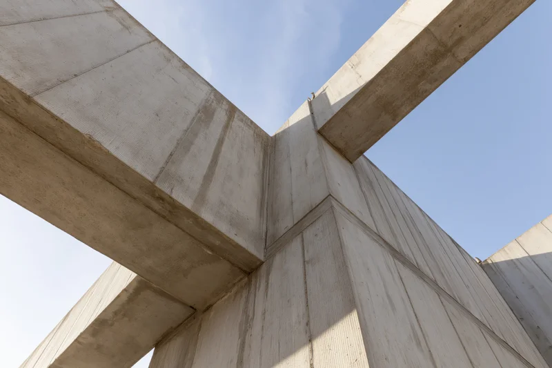 Brutalist concrete structure viewed from low angle showing intersecting beams and corner joint against blue sky