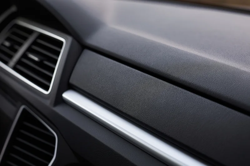 Closeup of car dashboard and glove box panel with air vents and chrome trim