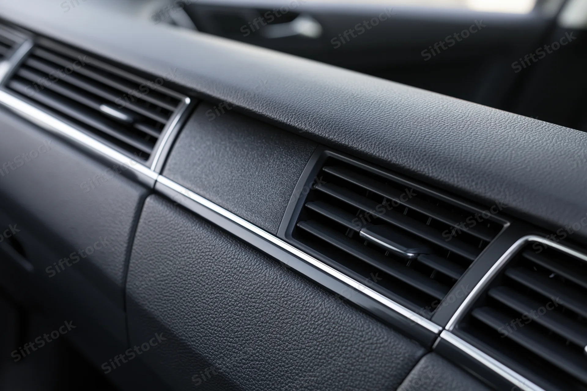 Closeup of car dashboard with air vents and chrome trim on black textured surface