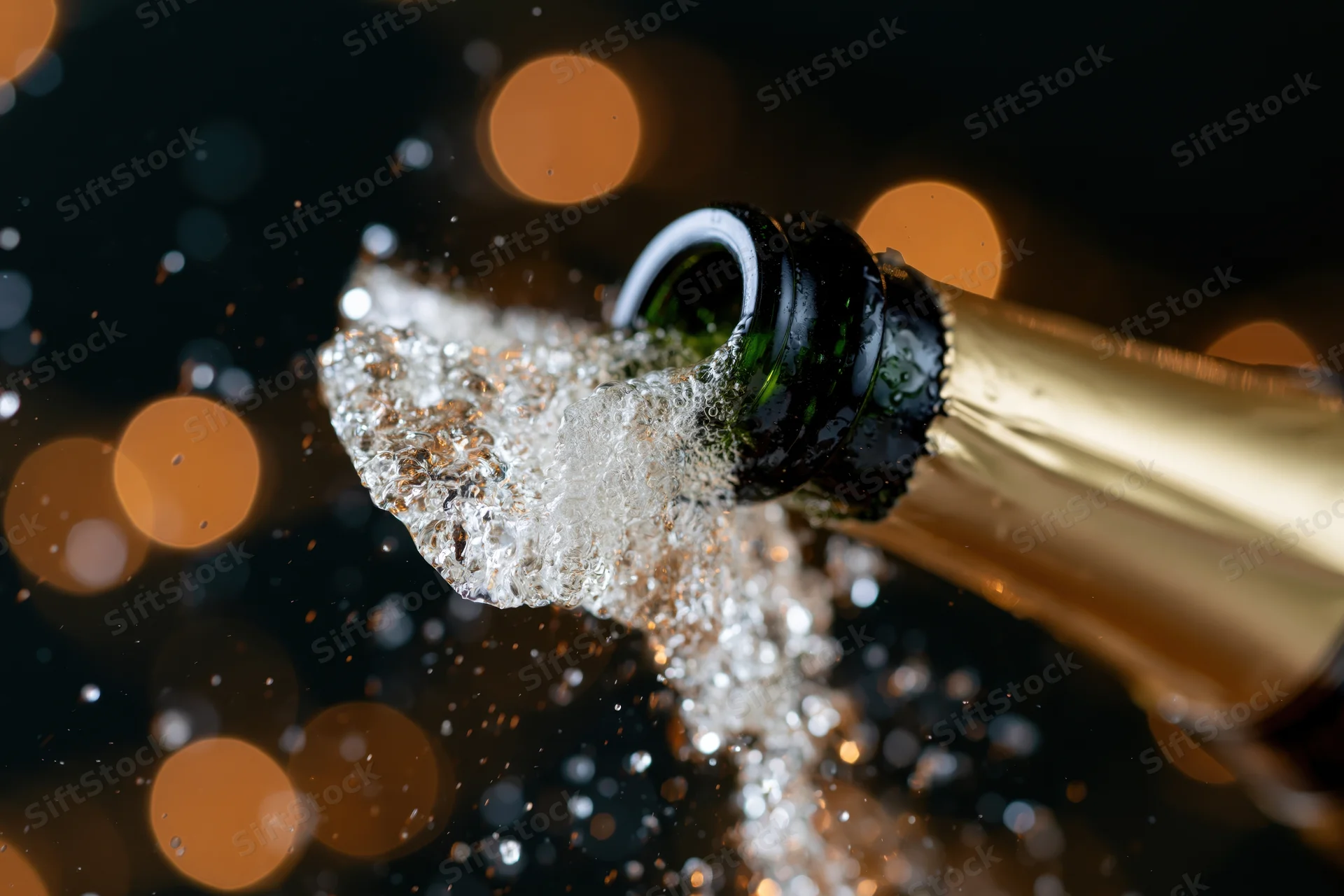 Champagne bottle neck tilted upward mid-pop with liquid droplets and bubbles spraying against dark bokeh background