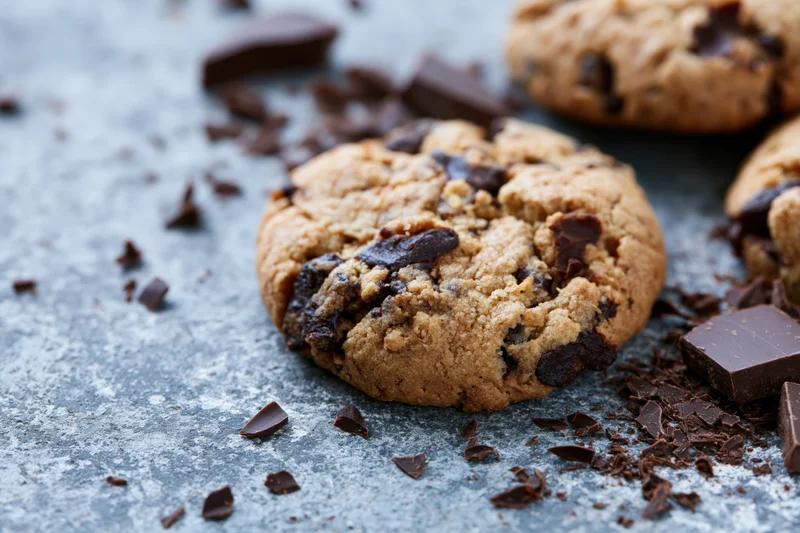 Chocolate chip cookies resting on a weathered grey concrete surface with scattered chocolate chunks around them