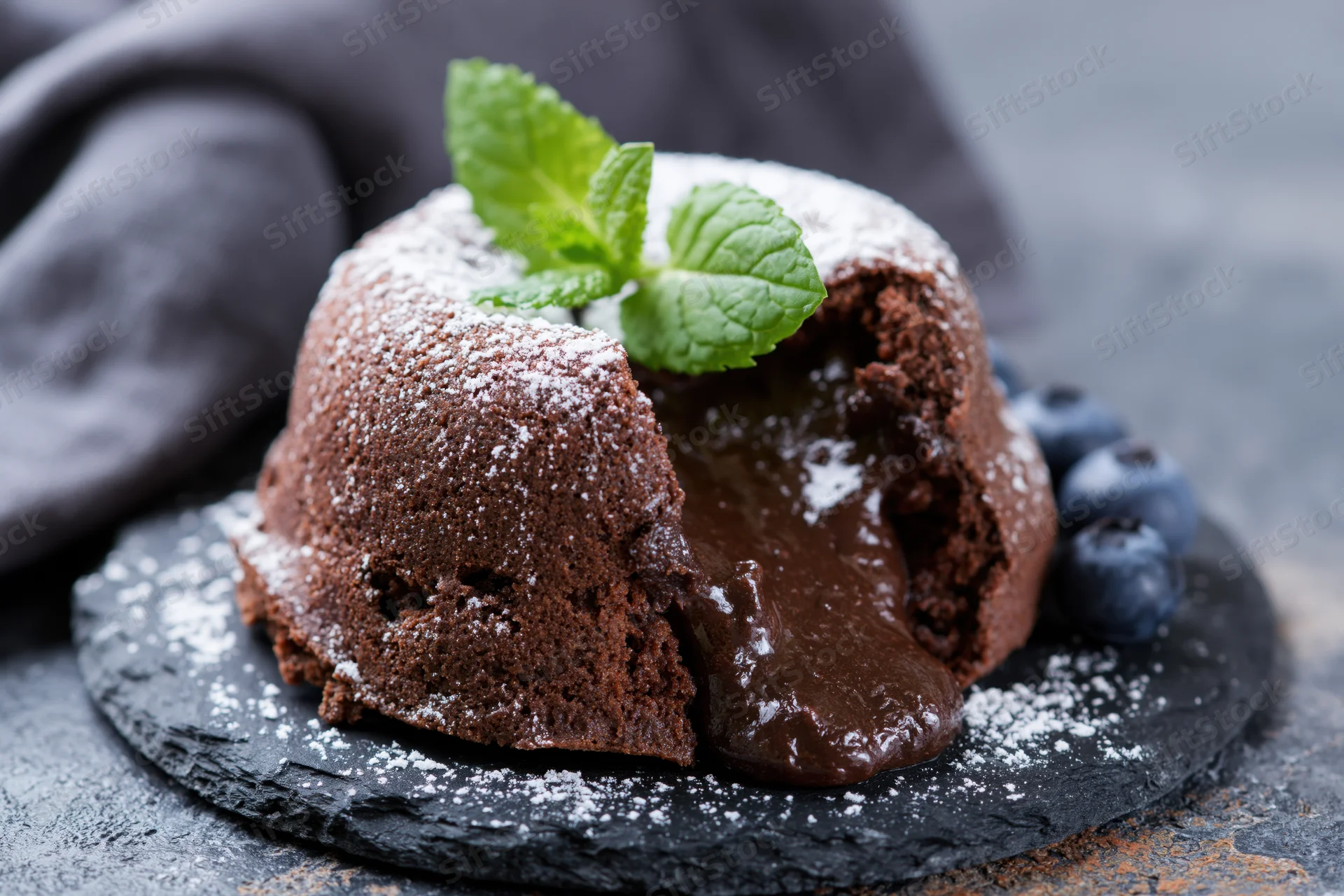 Chocolate lava cake with molten chocolate oozing from a break, served on slate with mint and blueberries