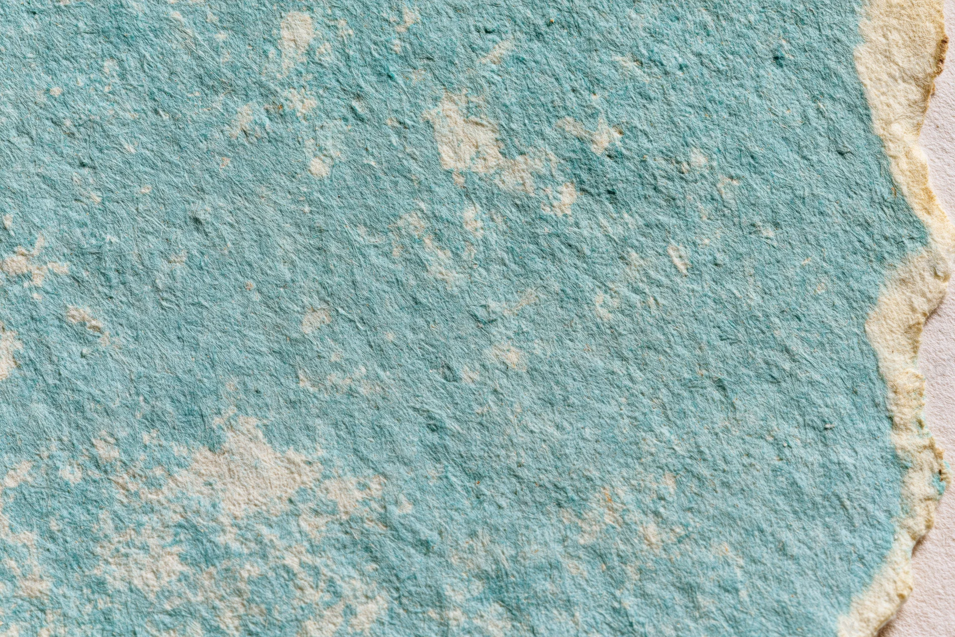 Close-up of aged turquoise paper surface with worn texture and torn edge