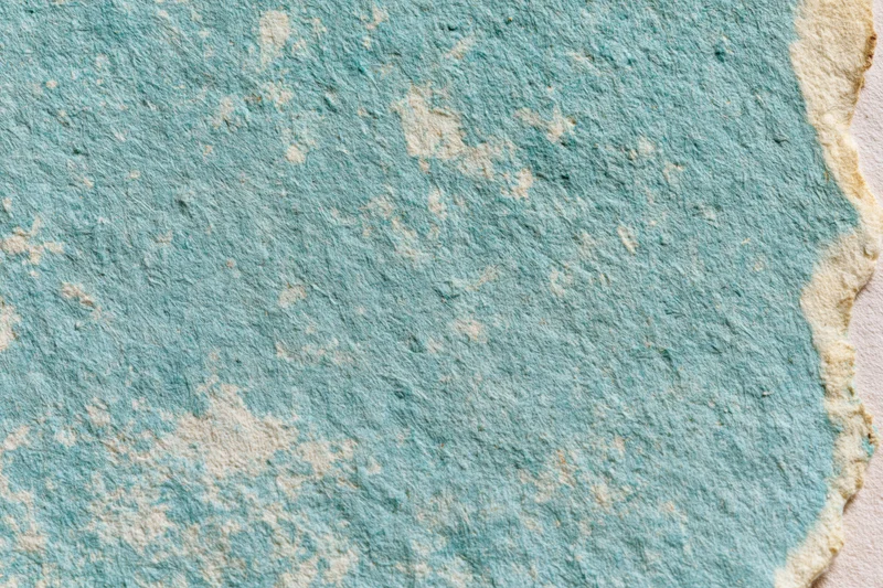 Close-up of aged turquoise paper surface with worn texture and torn edge