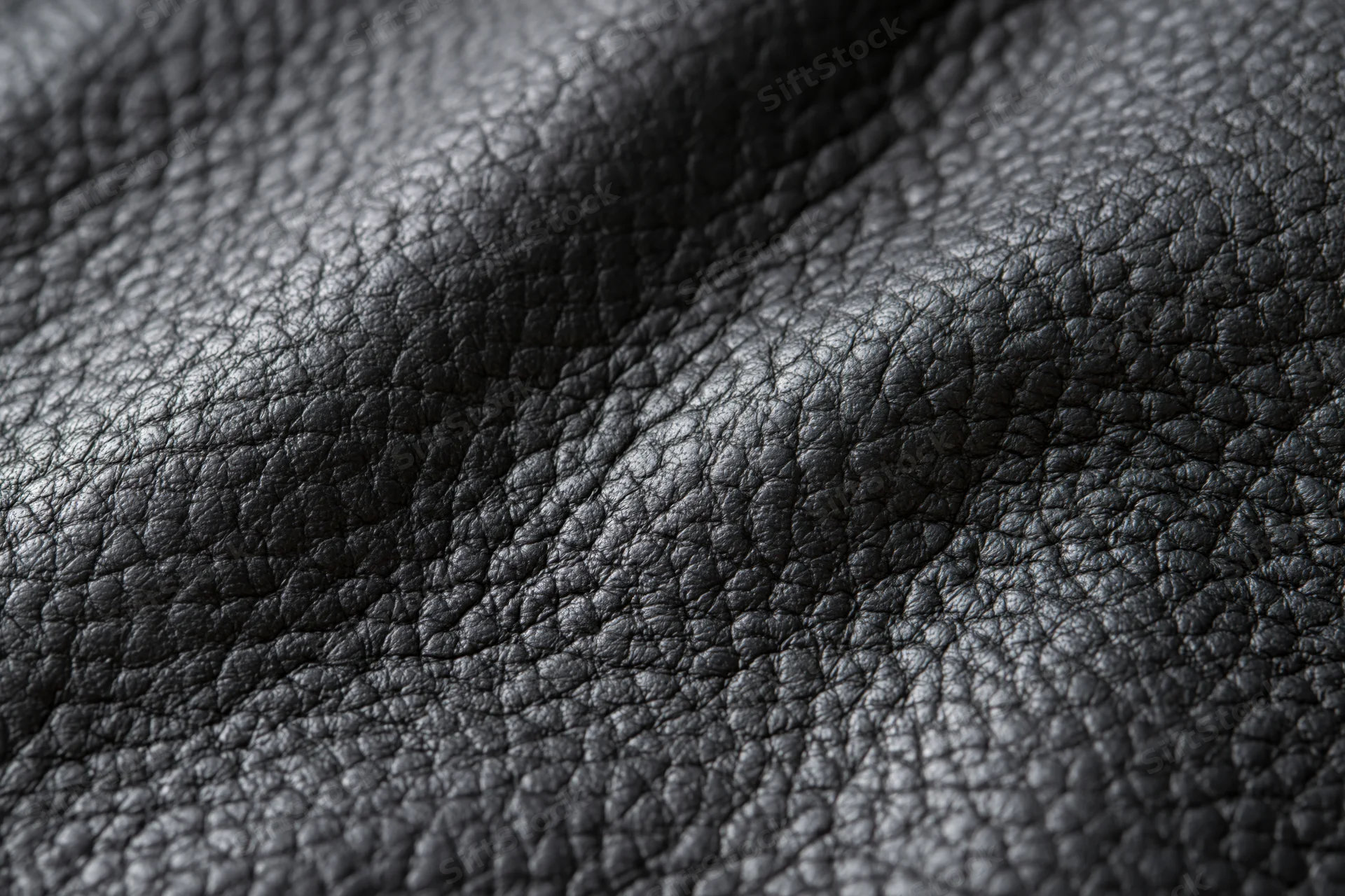 Close-up of black genuine leather surface with visible grain and folds filling the frame