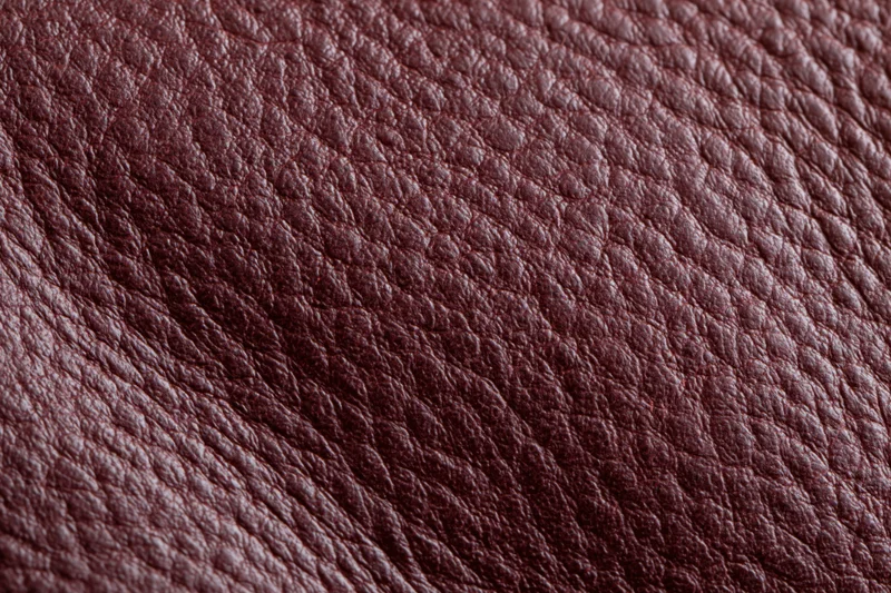 Close-up flat lay of deep burgundy genuine leather surface with visible grain texture