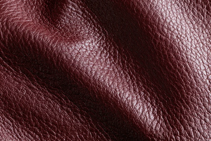Close-up of deep burgundy genuine leather surface with natural grain and folds