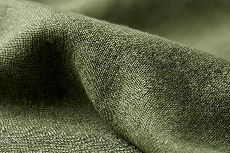 Close-up of olive green linen fabric with visible weave and folds filling the frame
