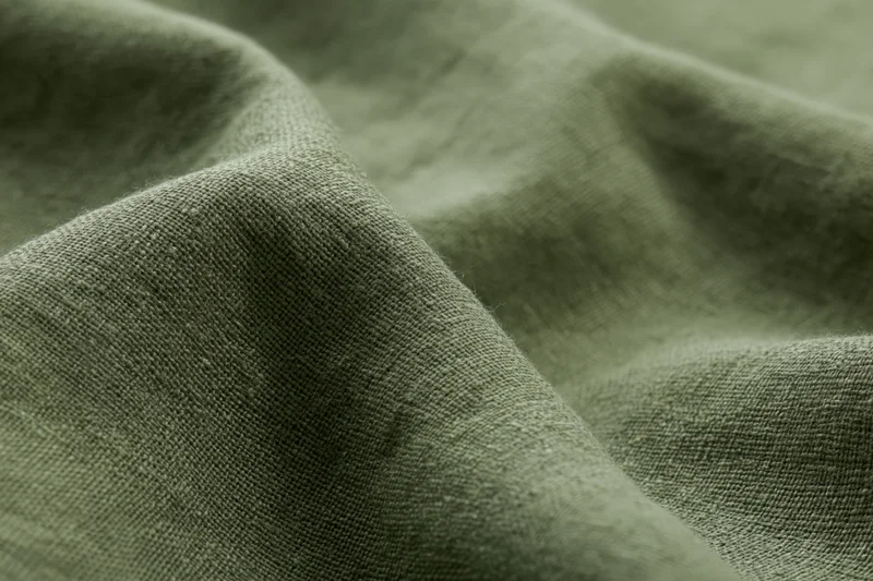 Close-up of olive green linen fabric with visible weave and soft folds filling the frame