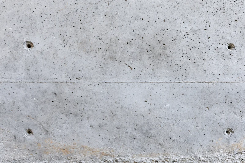 Close-up of a bare concrete wall surface with visible texture and formwork holes