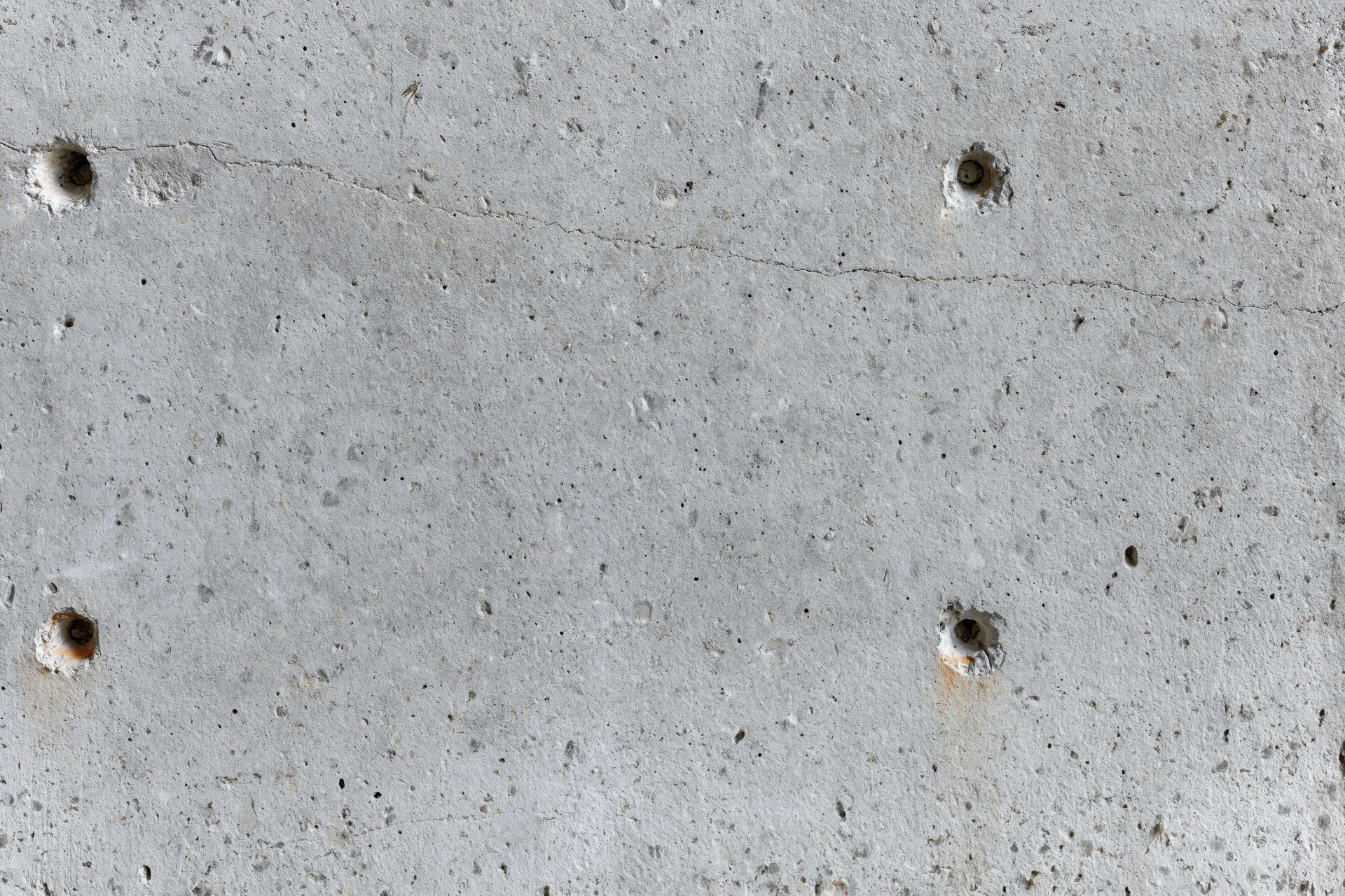 Close-up of a bare concrete wall surface with visible holes and cracks