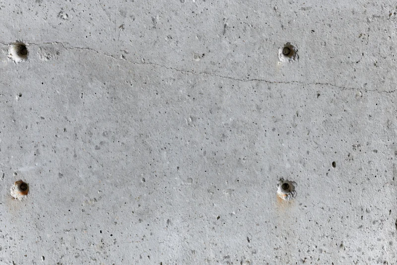 Close-up of a bare concrete wall surface with visible holes and cracks