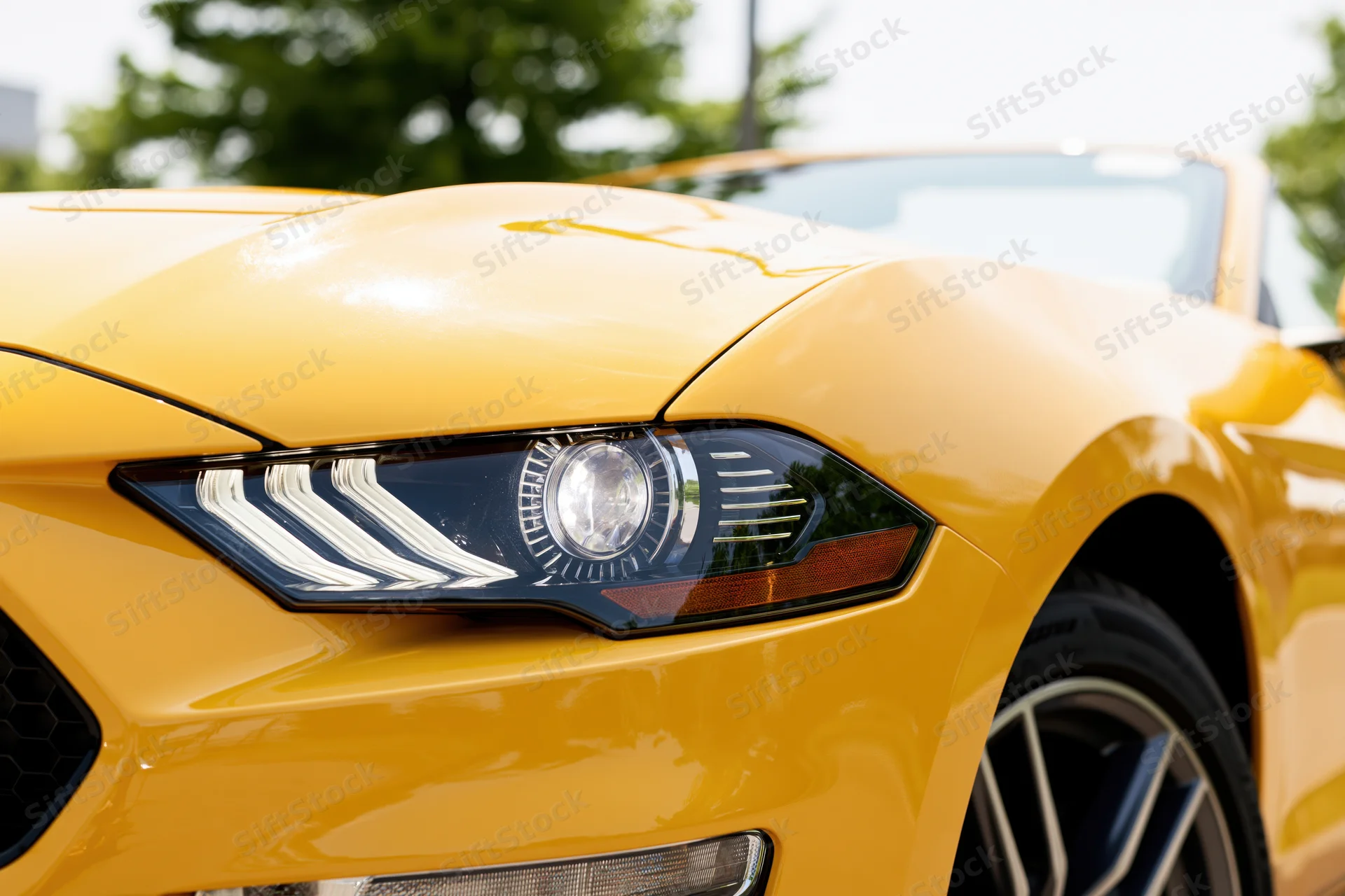 Close-up front quarter view of a yellow ford mustang convertible showing headlight and wheel outdoors