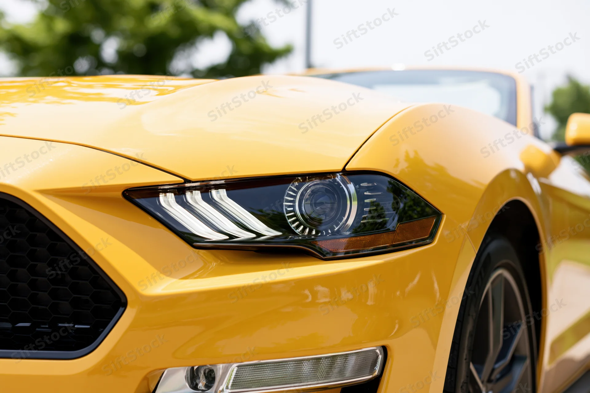 Close-up front quarter view of a yellow ford mustang convertible showing headlight grille and wheel