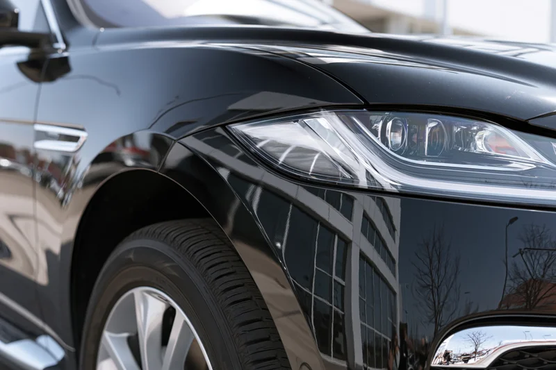Close-up of black luxury suv front corner showing headlight wheel and chrome grille with building reflection