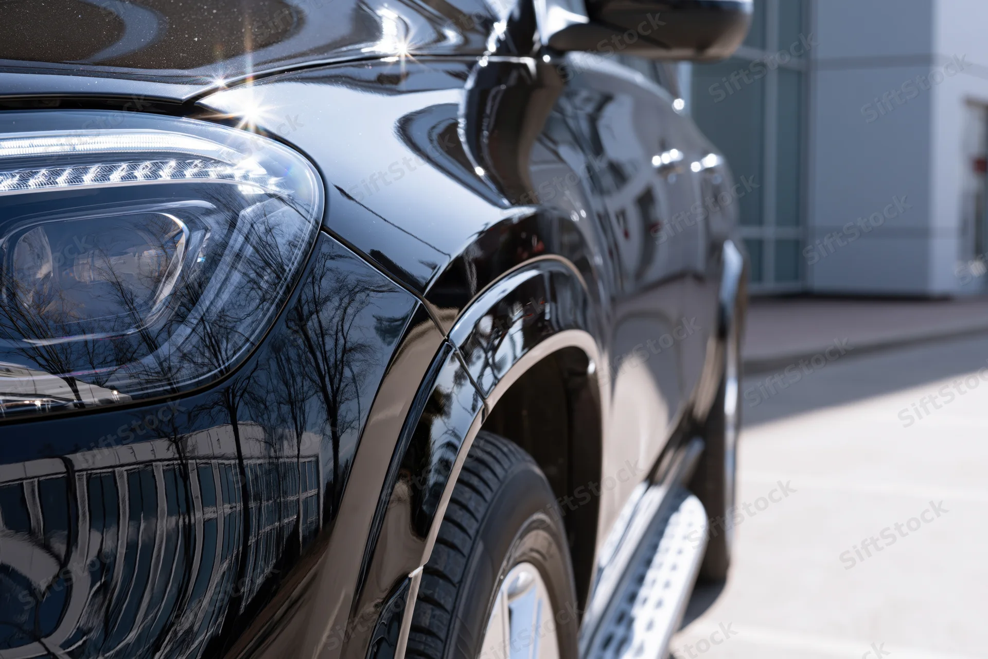 Close-up of black luxury suv front corner showing headlight grille and wheel on urban street