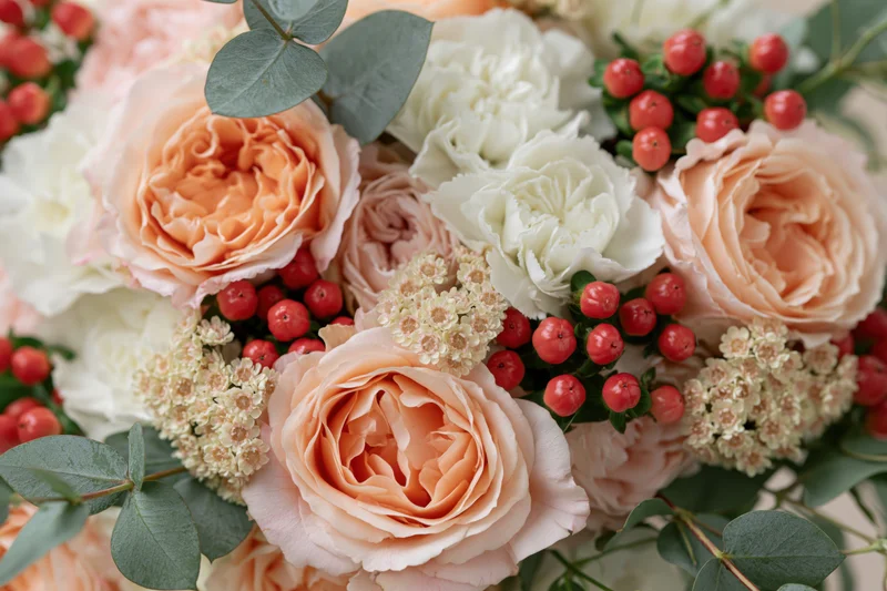 Close-up of a bridal bouquet with peach garden roses, white flowers, red berries and eucalyptus leaves