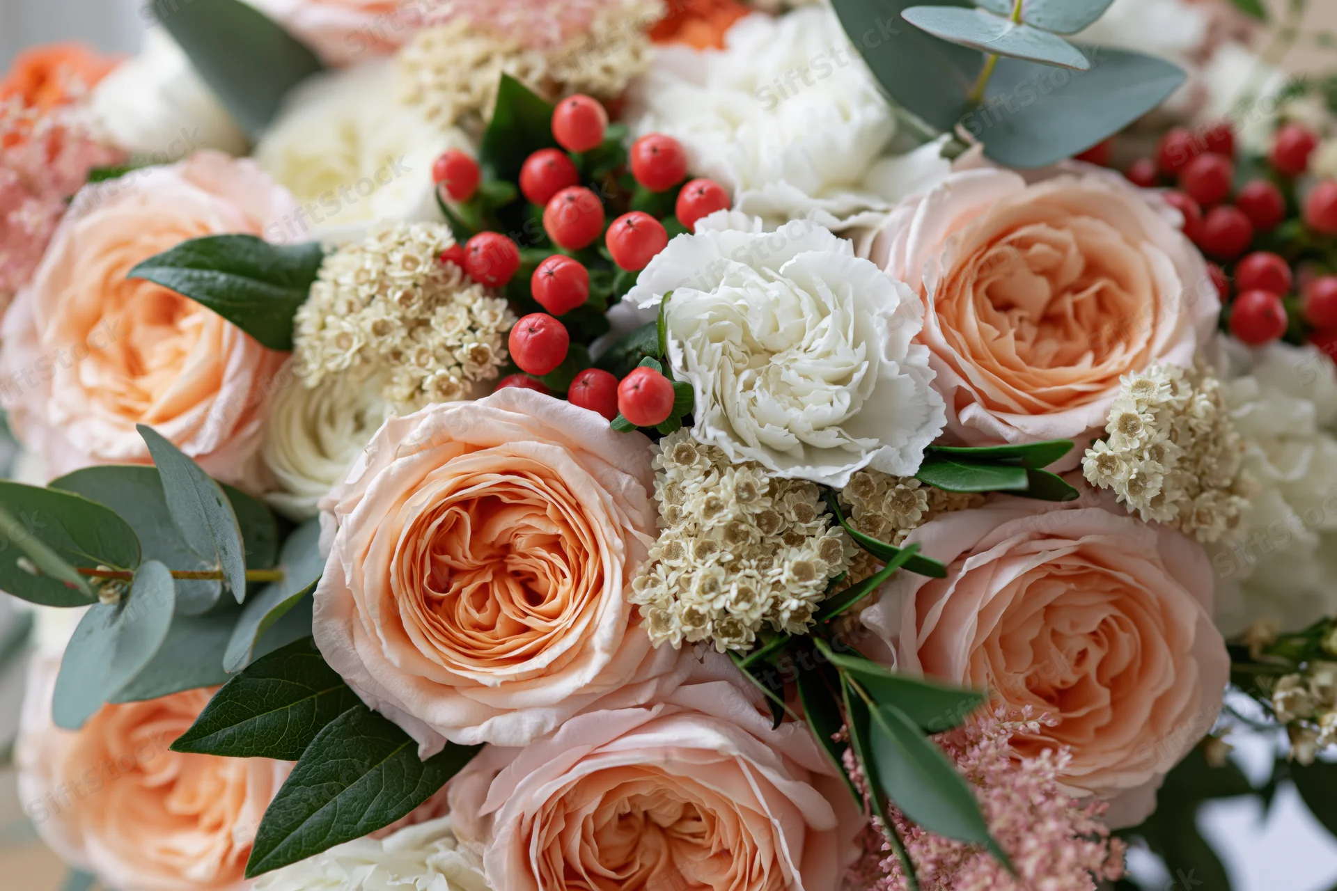Close-up of a bridal bouquet with peach garden roses, white flowers, greenery and red berries