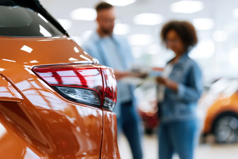 Close-up of copper-brown suv tail light in showroom with couple reviewing brochure in background