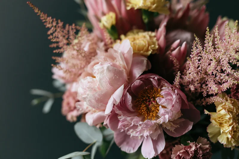 Close-up of a loosely arranged garden bouquet with pink peonies, yellow carnations, and astilbe against a dark background