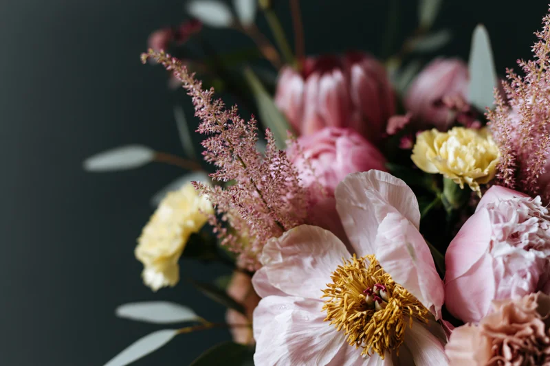 Close-up of a loosely arranged garden bouquet with pink peonies, yellow ranunculus, astilbe and eucalyptus foliage against a dark background