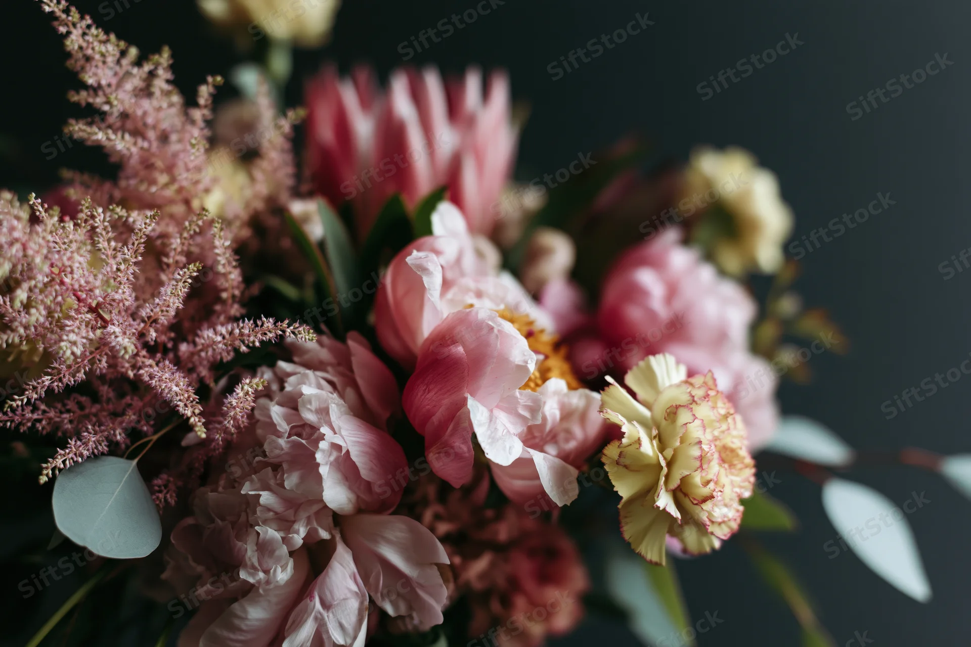 Loosely arranged garden bouquet with pink peonies, carnations, astilbe and eucalyptus foliage against dark background