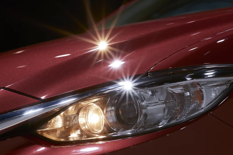 Close-up of a red car's projector headlight glowing against a dark background