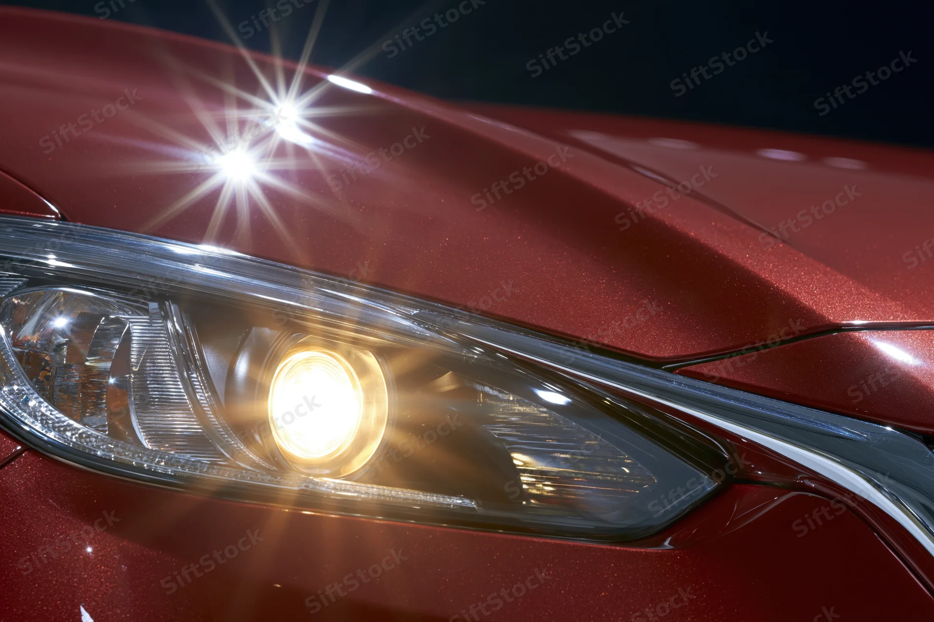 Close-up of a red car's projector headlight glowing against a dark background
