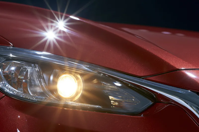 Close-up of a red car's projector headlight glowing against a dark background