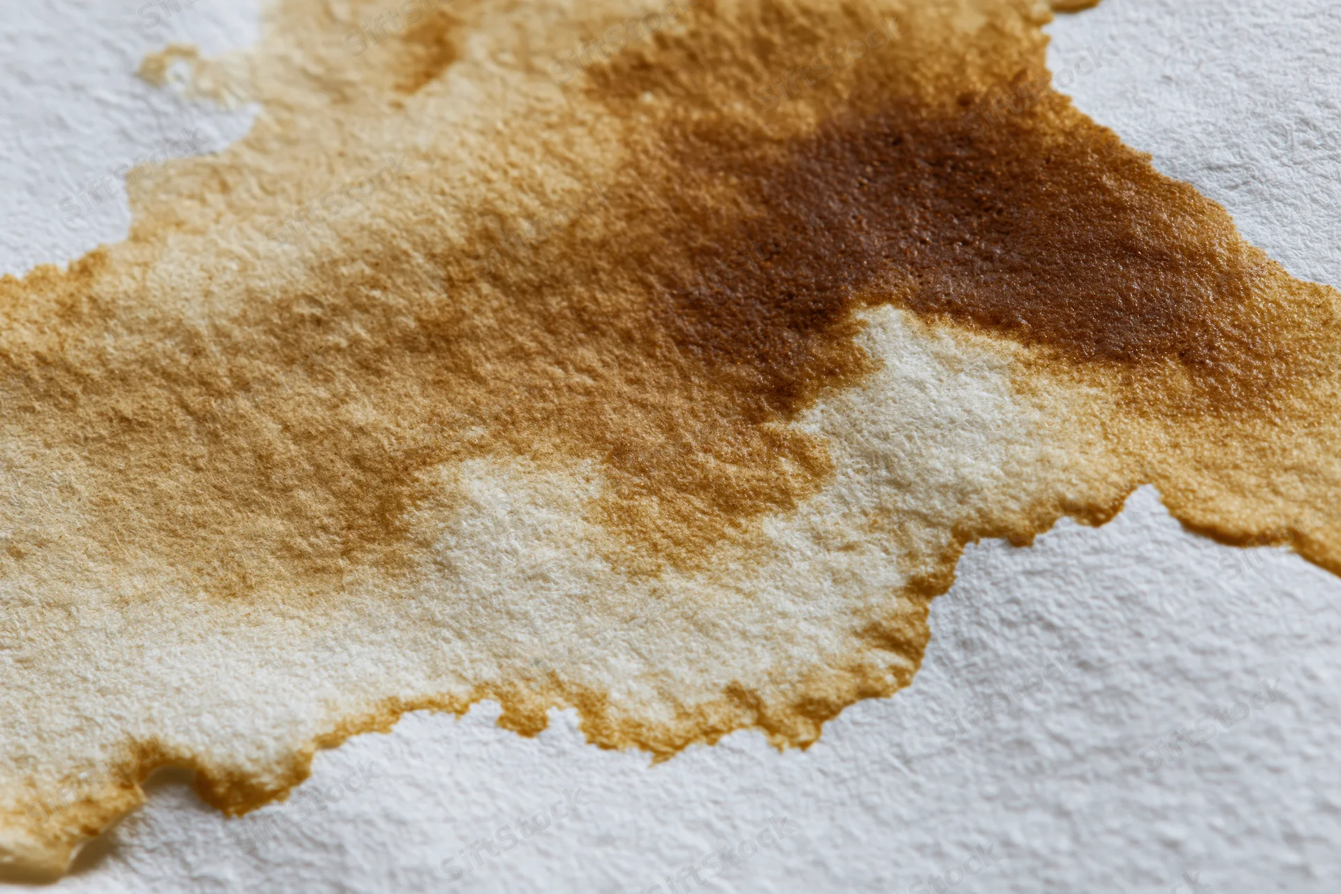Coffee or tea liquid stain spread across white watercolor paper surface