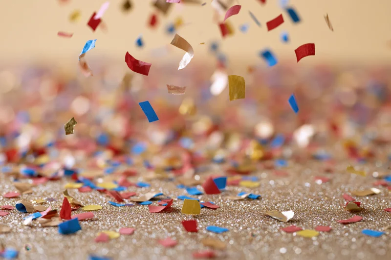 Colorful confetti and metallic foil pieces falling and scattered on a glittering gold surface
