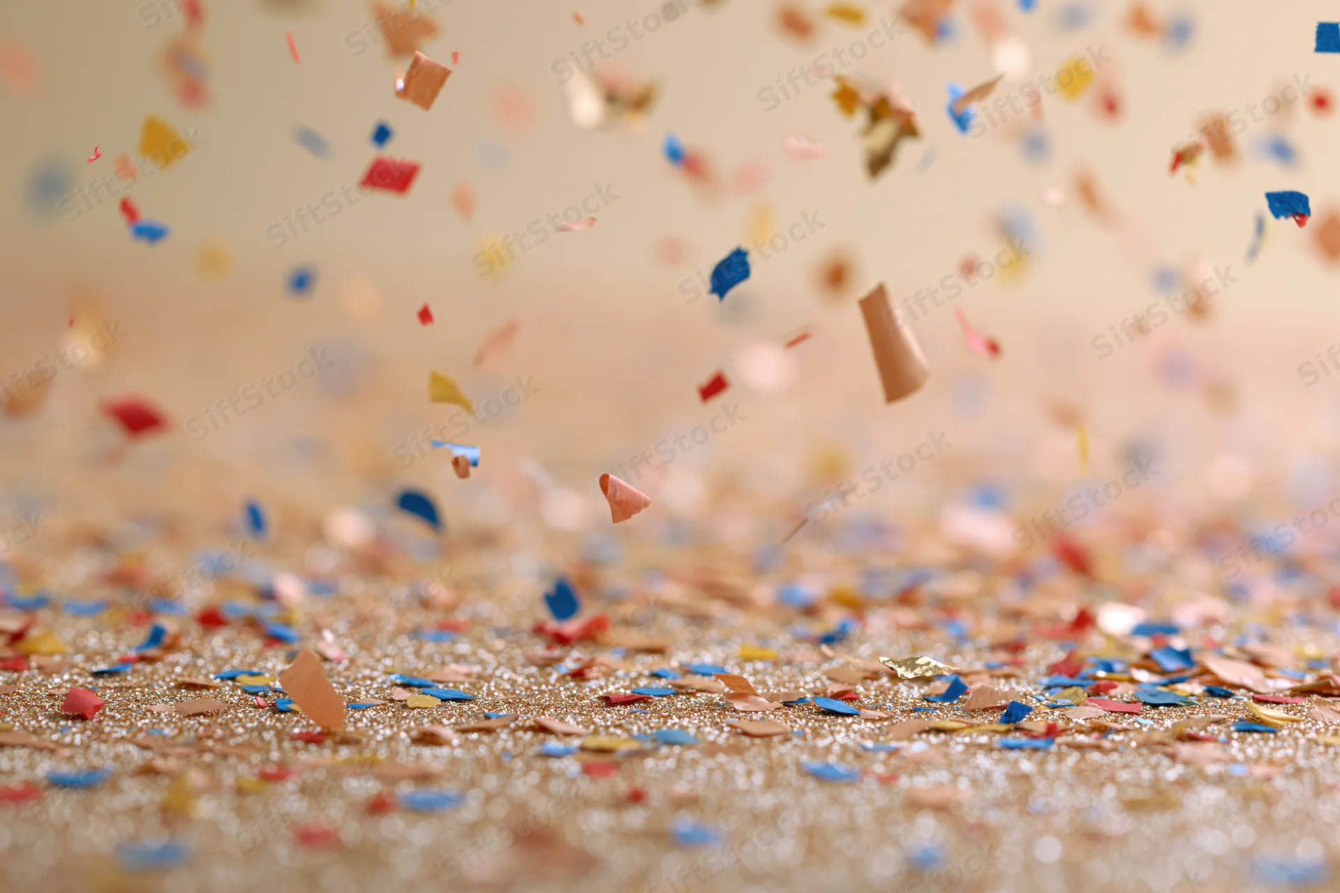 Colorful confetti and metallic foil pieces falling and scattered on a glittering gold surface