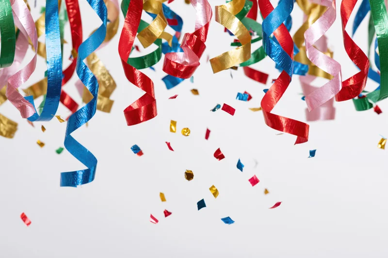 Colorful metallic party streamers and confetti falling against a white background with copyspace