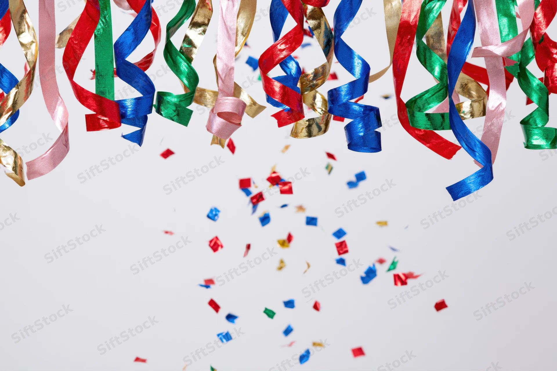 Colorful metallic party streamers and confetti falling against a white background with copyspace