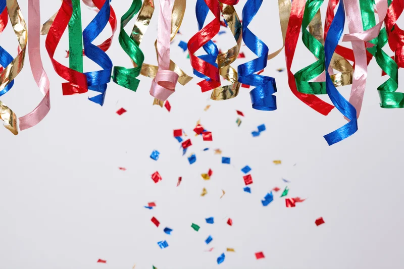 Colorful metallic party streamers and confetti falling against a white background with copyspace
