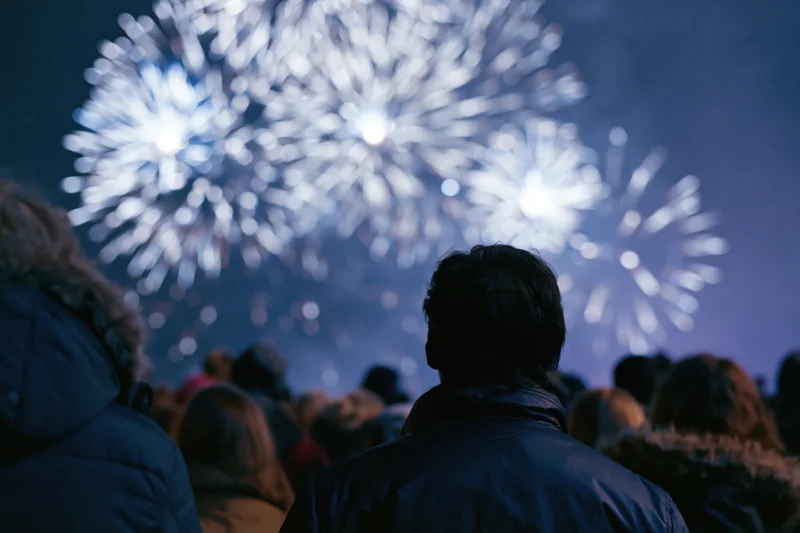 Crowd of people silhouetted from behind watching fireworks in the night sky