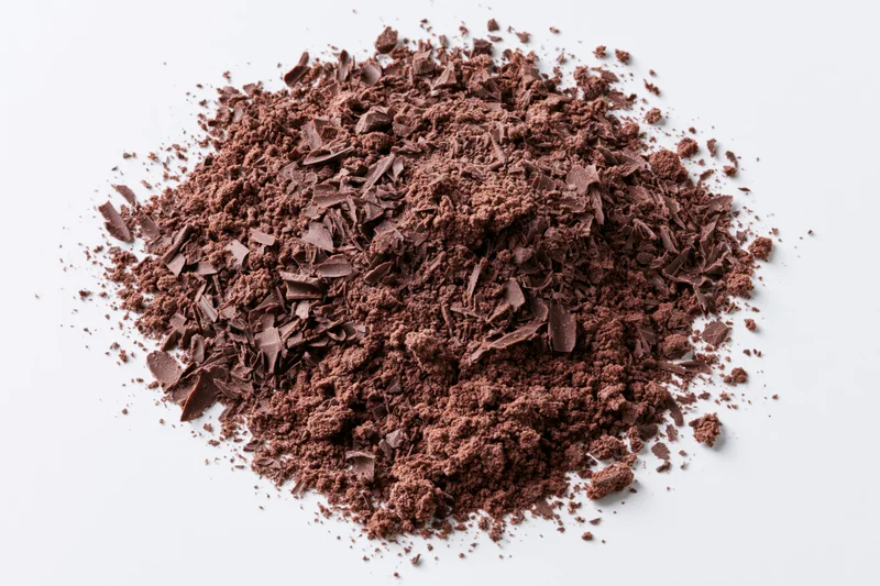 Dark chocolate shavings and coarse crumbles scattered in a pile on a white surface