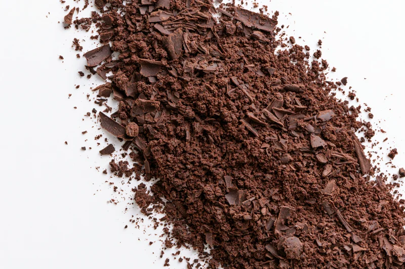 Dark chocolate shavings and coarse crumbles scattered across a white surface