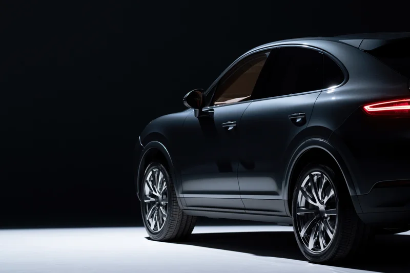 Dark grey luxury suv shown from rear threequarter angle in studio lighting with white floor and black background