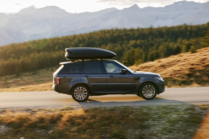 Dark grey luxury suv with black rooftop cargo box driving on mountain road at sunset