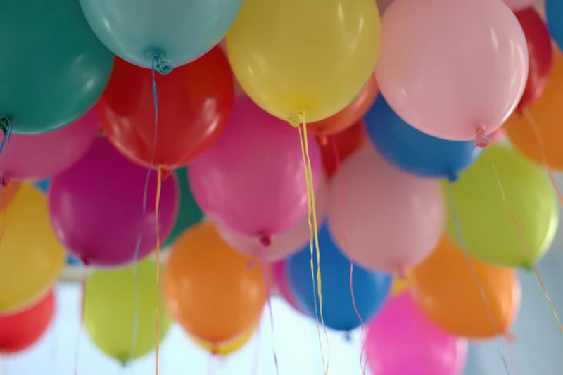 Dozens of colorful helium balloons floating against a ceiling with strings attached