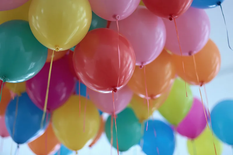 Dozens of helium balloons floating against a ceiling with strings attached