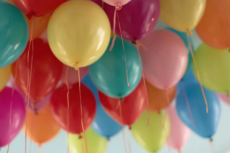 Dozens of colorful helium balloons floating against a ceiling with strings hanging down