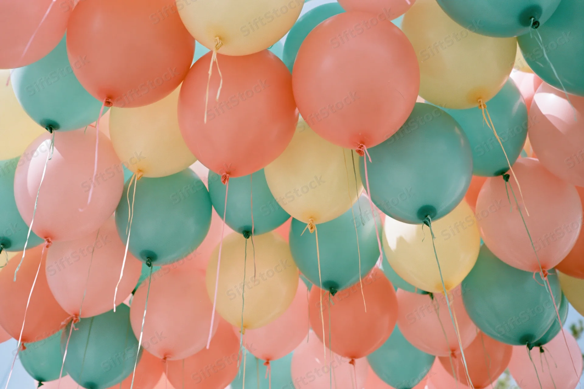 Cluster of inflated balloons in coral pink teal and soft yellow floating outdoors as party decoration