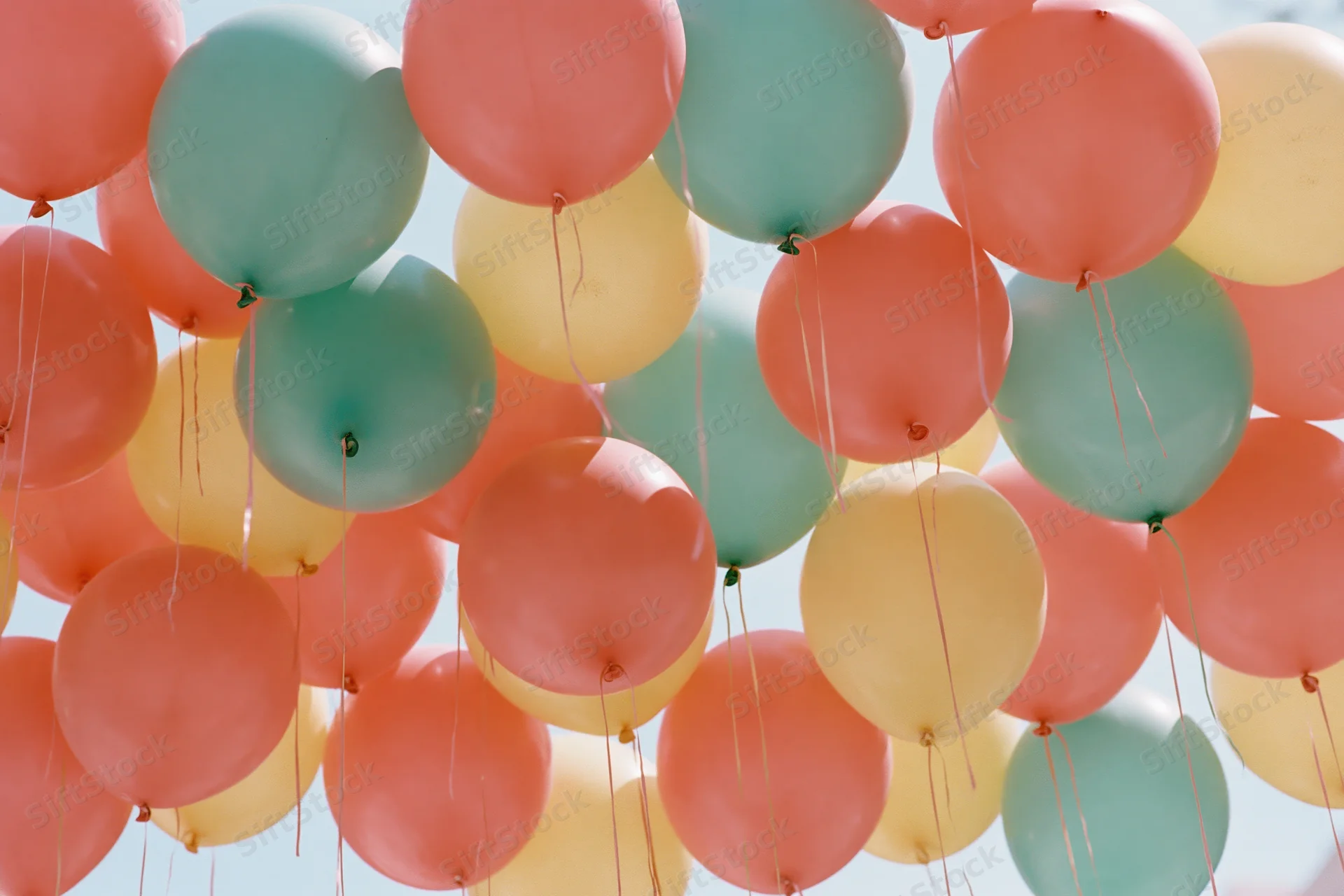 Dozens of inflated balloons in coral pink teal and soft yellow floating against sky