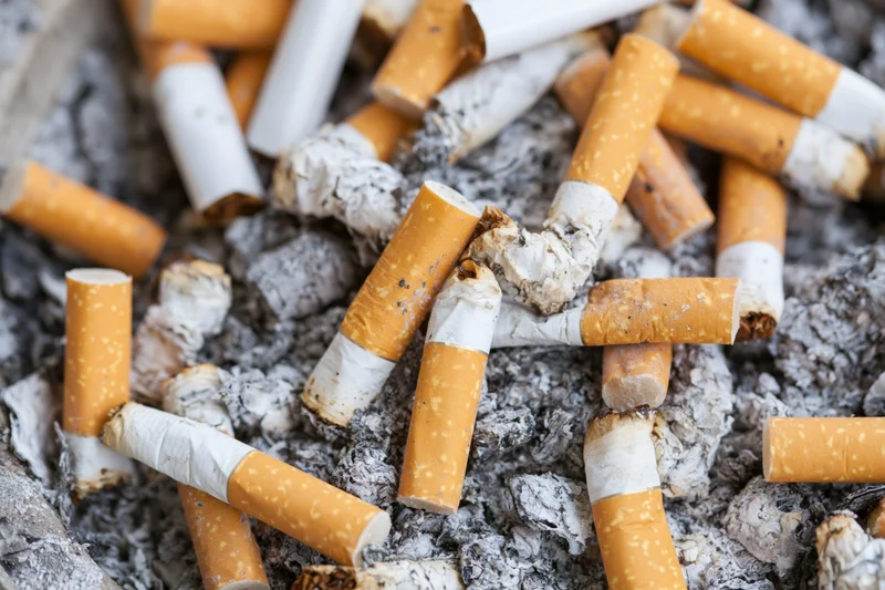 Cigarette butts piled in a public ashtray filled with ash and debris
