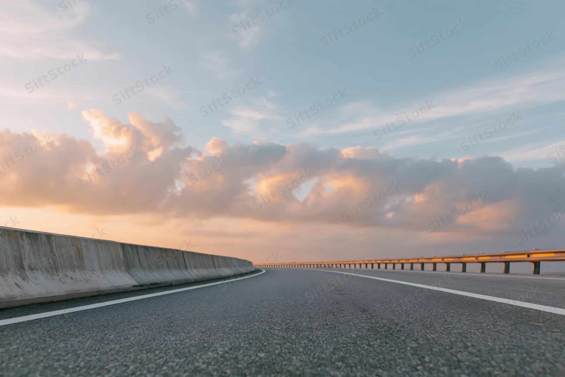 Empty curved asphalt highway sweeping right with guardrails under sunset sky